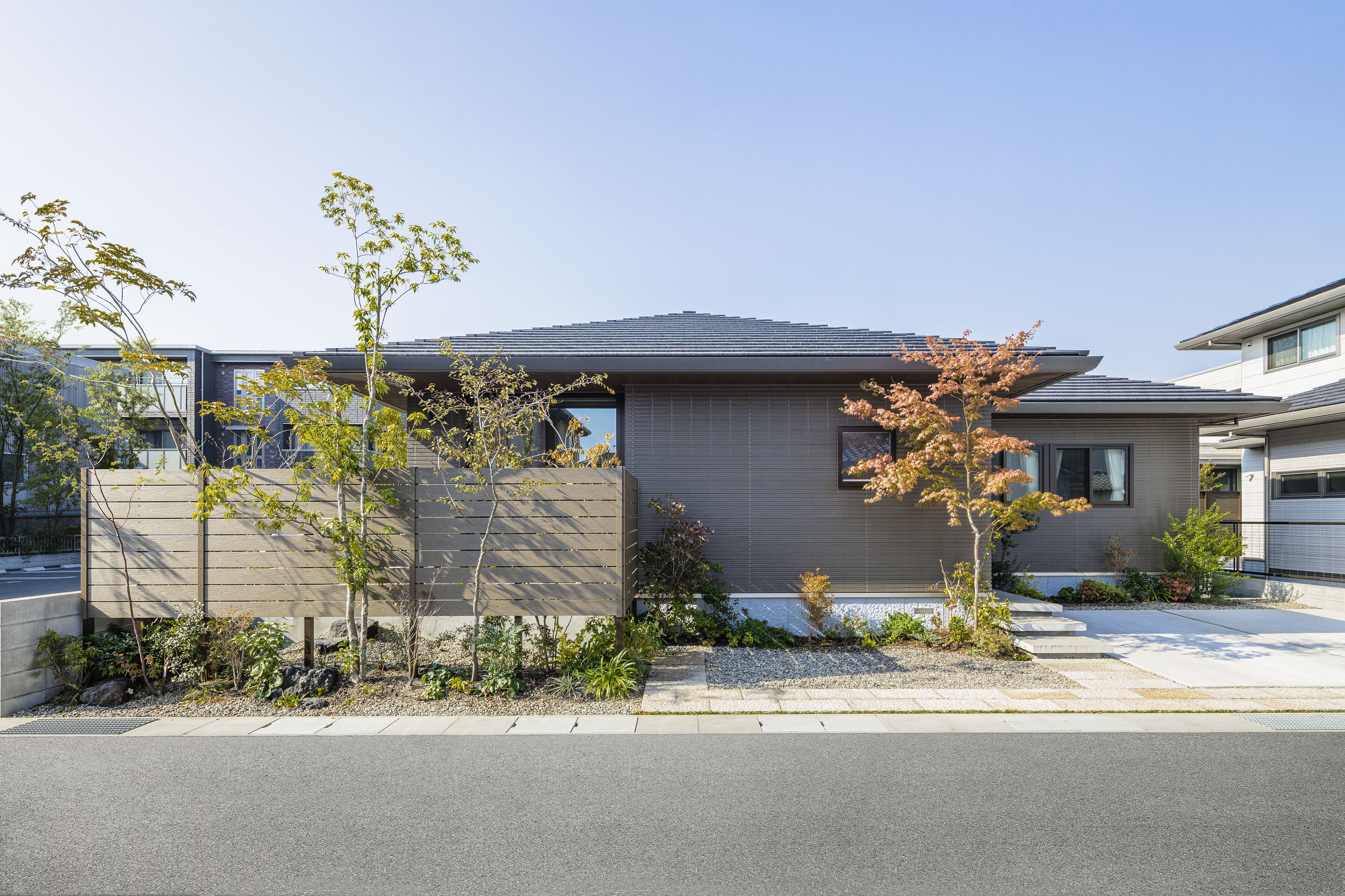 寄棟屋根と、濃色の陶板外壁ベルバーンを組み合わせたシンプルな外観。庭やアプローチに配した植栽が、より街並みに映える