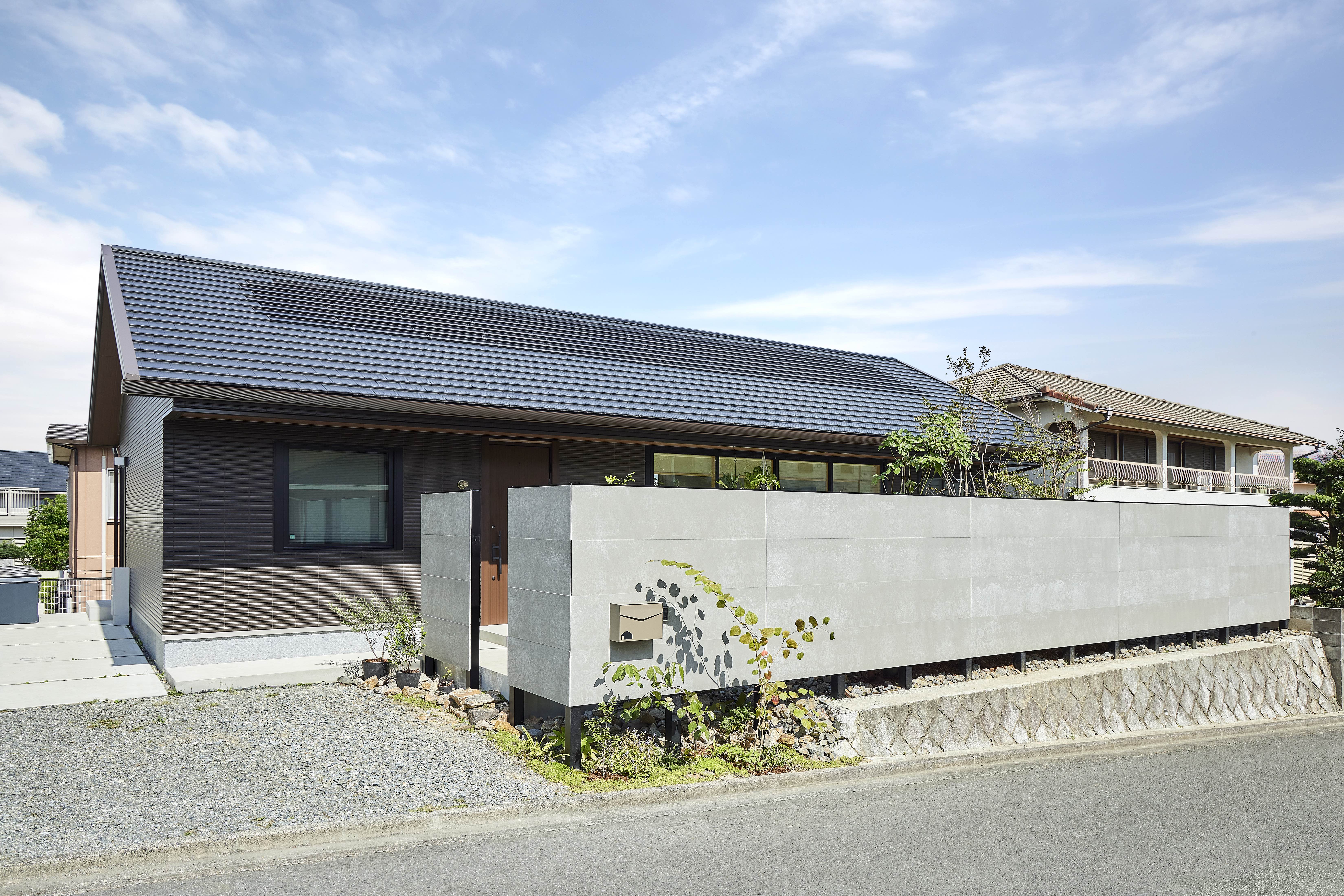 周辺環境と調和する平屋の外観。セメントや古紙パルプなど再生可能な材料からつくられたやさしい質感の壁材を外塀に使用している